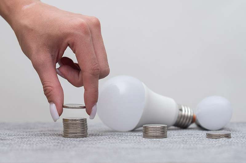 woman's hand adding a coin to a pile of coins with 2 LED bulbs in the background