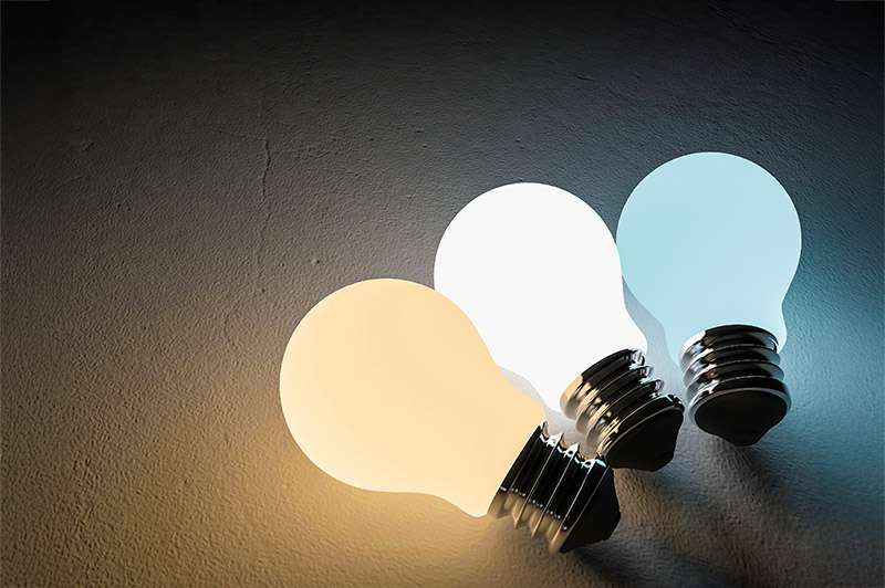 3 light bulbs on a table, one in warm white, one cool white and one daylight.