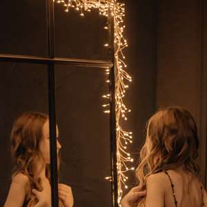 A beautiful little girl in a tight-fitting, shiny dress is standing by the mirror. The concept of children's style and fashion. The child is going to celebrate a birthday. Reflection of a child in the mirror.
