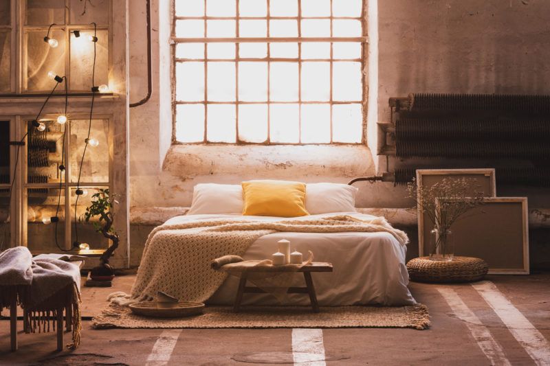 Real photo of a cozy, industrial bedroom interior with a double bed, yellow pillow, window and chain lights
