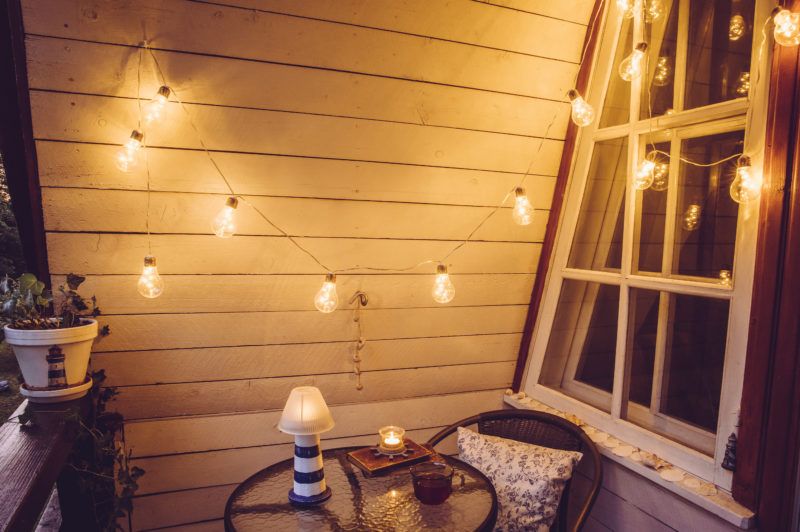 Cute retro wooden nautical style balcony view with small garden table and chair and decorative string party bulbs lights on in the evening.